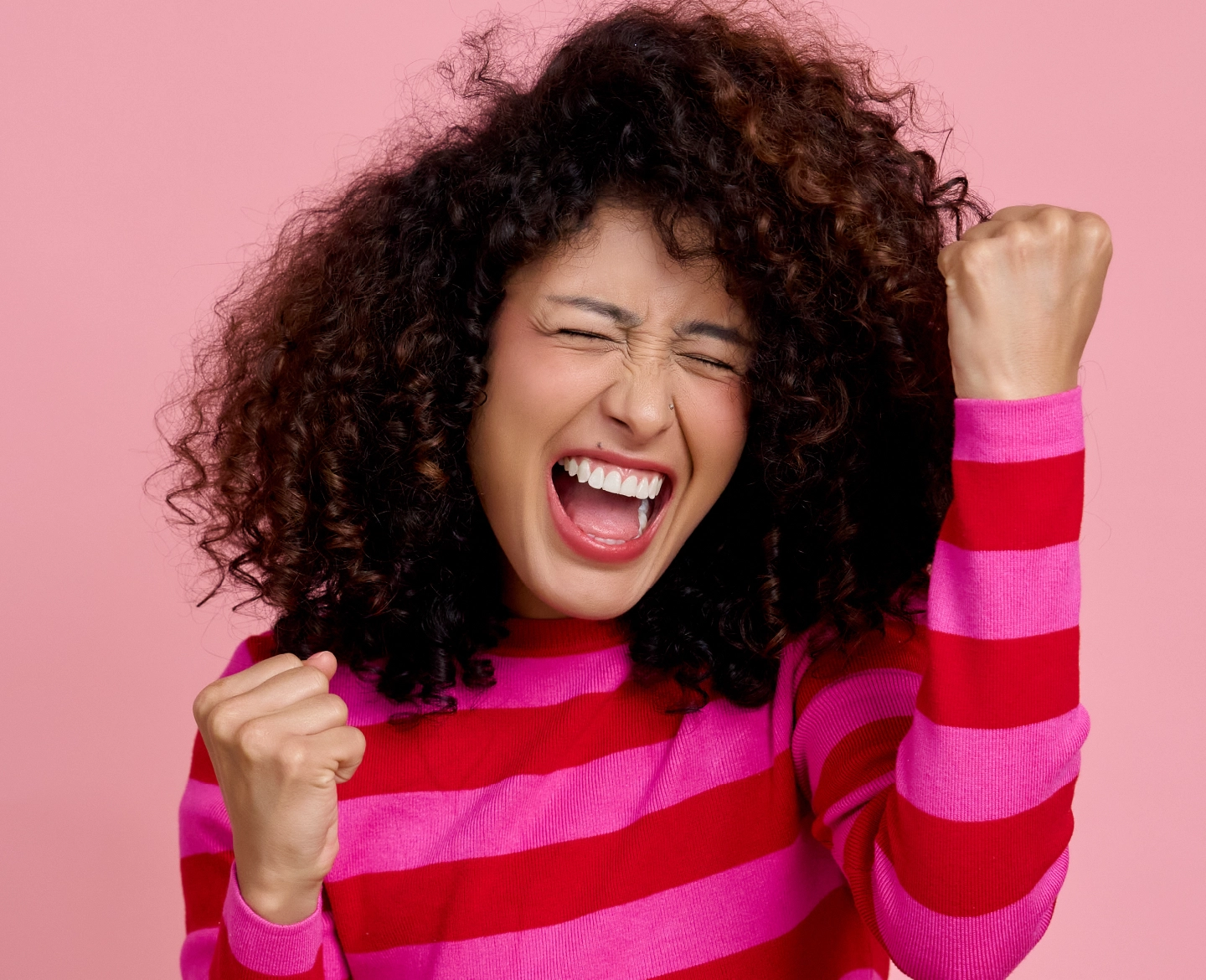 Pessoa em pose de celebração, com os braços levantados e fundo rosa.