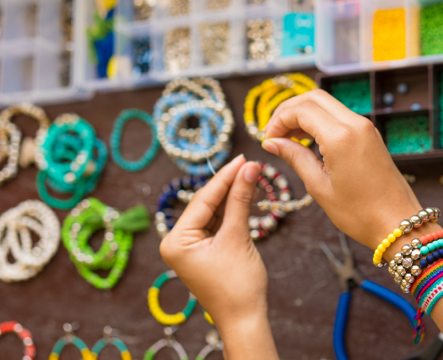 Mãos a criar pulseiras artesanais coloridas numa banca de acessórios feitos à mão.